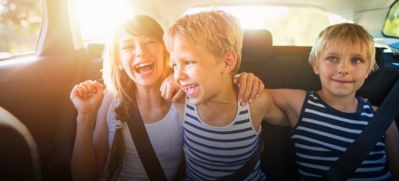 Trois enfants souriants profitant de leur voyage sur la banquette arrière de la voiture